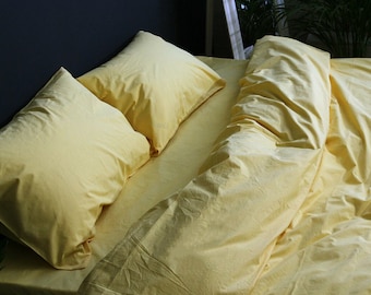 May include: A bed with yellow bedding, including two pillows and a duvet. The sheets and pillowcases are a solid, pale yellow color. The bed is in a room with a dark blue wall and a mirror.