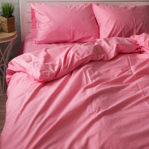 Puede incluir: Un juego de cama rosa que incluye una sábana bajera, dos fundas de almohada y una funda nórdica. La ropa de cama es de color rosa liso y vibrante, creando un aspecto cohesivo y acogedor. Las sábanas están cuidadosamente colocadas, sugiriendo un dormitorio cómodo y elegante.