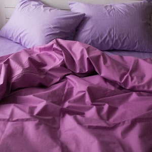 Könnte beinhalten: Ein Bett ist mit einem Satz lila Bettwäsche gemacht. Das Set enthält zwei Kissenbezüge und eine Bettdecke. Die Laken und Kissenbezüge sind heller als die Bettdecke. Die Bettwäsche ist aus einem weichen, knitterarmen Stoff.