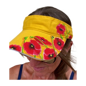 May include: A yellow visor with a white brim and a hand-painted design of red poppies.