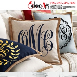 Puede incluir: Dos almohadas beige con ribete de yute y una almohada azul marino con un diseño de hojas doradas y un monograma. Las almohadas están en un sofá blanco. Un camino de mesa con un monograma blanco está en una mesa con dos vasos de vidrio transparentes.