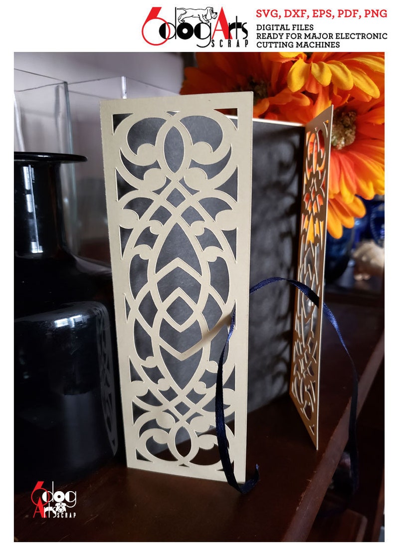 May include: A beige card with a decorative cut-out design. The card is folded in half and has a blue ribbon tied around it. The card is sitting on a wooden surface.