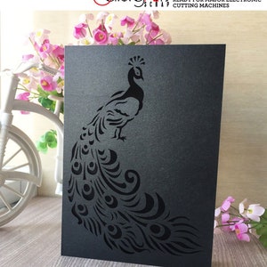May include: A black cardstock peacock design with intricate cut-out details. The peacock is standing with its tail feathers fanned out. The cardstock has the text "SVG, DXF, EPS, PNG CUTTING FILES READY FOR MAJOR ELECTRONIC CUTTING MACHINES".