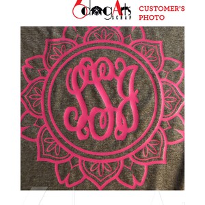 May include: A gray t-shirt with a pink mandala design and a pink monogram in the center. The monogram is the letters "S.S.G."
