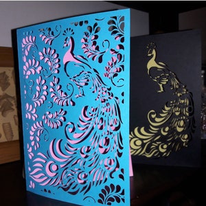 May include: Two laser-cut peacock greeting cards. One is turquoise with pink accents, the other is black with gold accents. The cards feature intricate feather and floral designs. Text on the top reads "SVG, DXF, EPS, PNG CUTTING FILES READY FOR MAJOR ELECTRONIC CUTTING MACHINES."