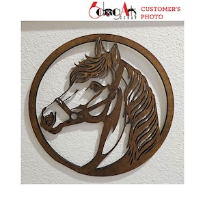 Pode incluir: Silhueta de cabe&ccedil;a de cavalo em madeira dentro de uma moldura circular. O perfil do cavalo &eacute; intrincadamente cortado, mostrando a crina, o olho e a brida. A obra de arte &eacute; de cor castanha quente e est&aacute; montada numa parede branca. O texto "CUSTOMER'S PHOTO" &eacute; vis&iacute;vel.