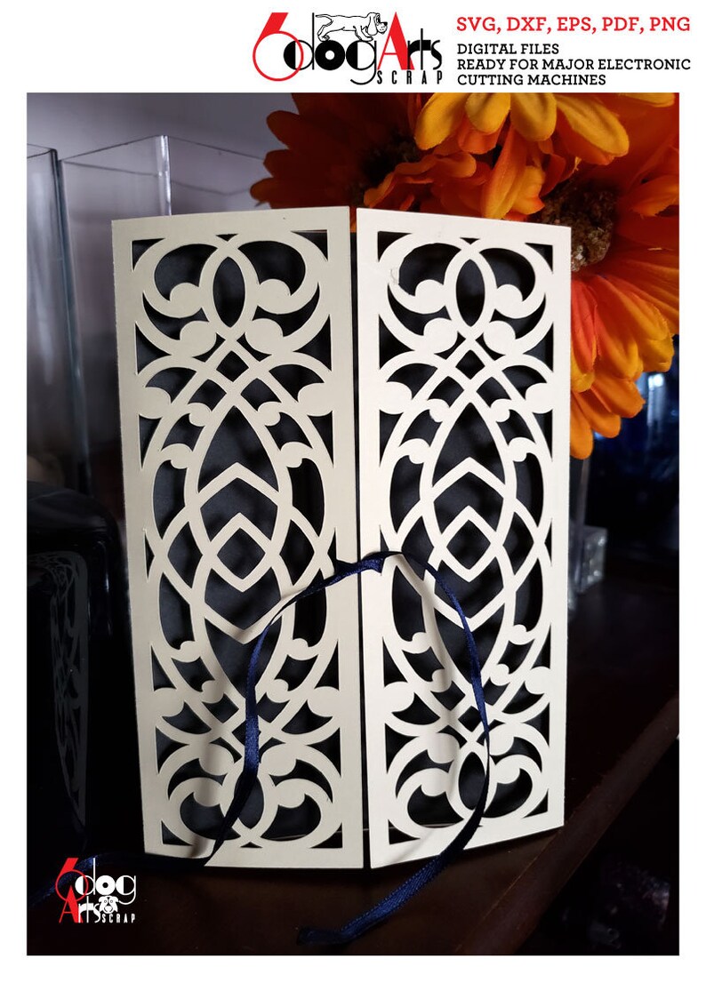 May include: A white cardstock die cut with a decorative, intricate design. The cardstock is folded in half and tied with a blue ribbon. The cardstock is on a wooden surface.