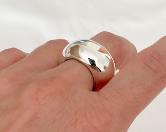 May include: A silver ring with a rounded, smooth design. The ring is thick and has a wide band.