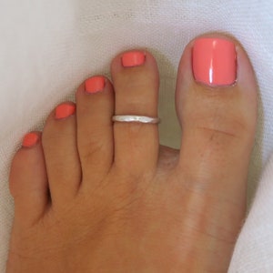 Peut inclure: Gros plan d'un pied avec une bague d'orteil argentée. Les orteils sont peints d'un vernis à ongles corail vif.