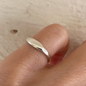 May include: A silver ring with a smooth, elongated oval design. The ring is worn on a finger, showcasing its polished, reflective surface. The ring's simple, elegant style makes it suitable for everyday wear.