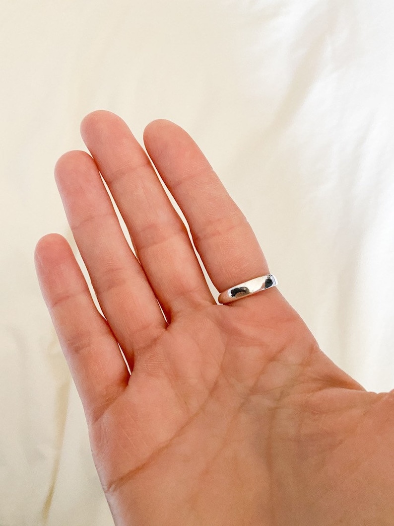 K&ouml;nnte beinhalten: Ein silberner Bandring an einem Finger.