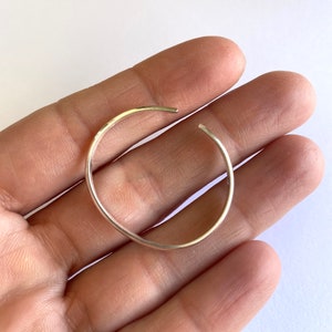 Peut inclure: Un bracelet jonc en argent simple, présenté sur une main, avec une finition lisse et arrondie.