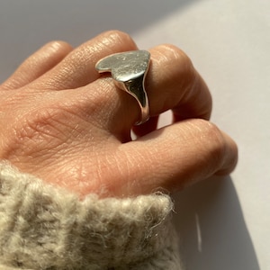 K&ouml;nnte beinhalten: Ein silberner Ring in Herzform mit einer glatten, leicht strukturierten Oberfl&auml;che.