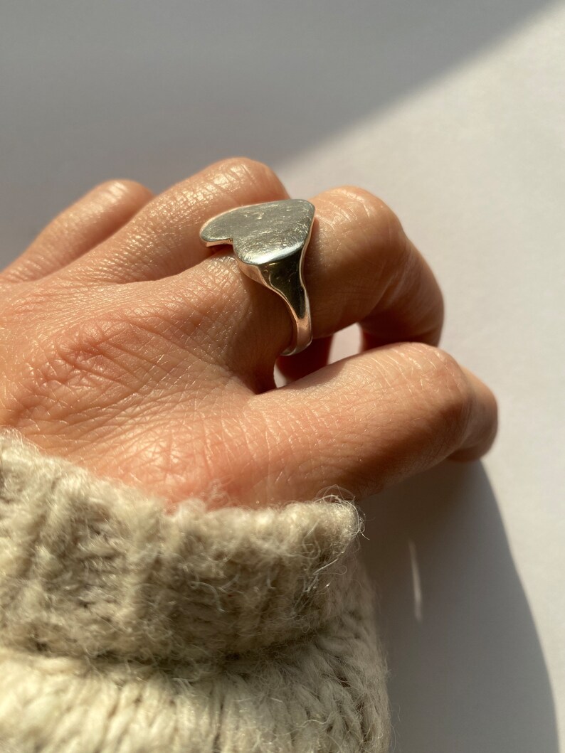 K&ouml;nnte beinhalten: Ein silberner Ring in Herzform mit einer glatten, leicht strukturierten Oberfl&auml;che.