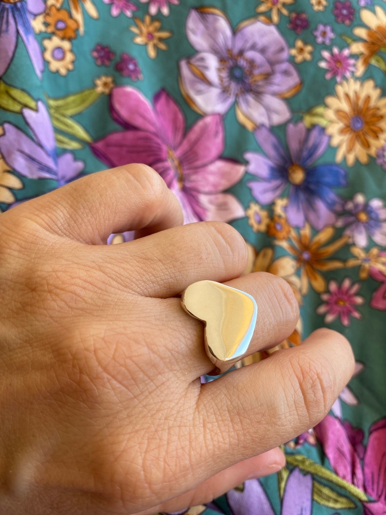 K&ouml;nnte beinhalten: Ein silberner Ring in Herzform an einem Finger.