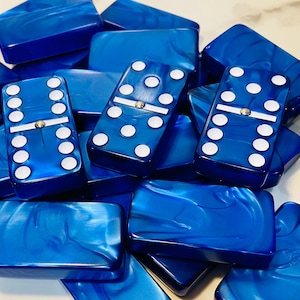 May include: A collection of blue dominoes with white dots and a central white bar. The dominoes have a glossy finish and a marbled appearance. The game pieces are scattered, showing various dot combinations.