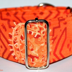 Puede incluir: Collar para perro de color naranja y rojo con un diseño geométrico y una hebilla plateada. El collar está hecho de tela.