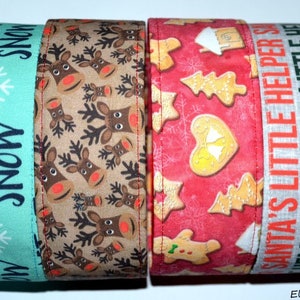 Puede incluir: Cuatro cintas de tela con temática navideña. Una es turquesa con copos de nieve y el texto "LET IT SNOW". Otra es beige con renos. La tercera es roja con hombres y árboles de jengibre. La última es blanca con el texto "SANTA'S LITTLE HELPER".