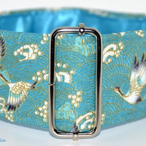 Puede incluir: Un collar para perro azul turquesa con una hebilla plateada. El collar presenta un patrón repetitivo de grullas blancas y olas sobre un fondo azul.