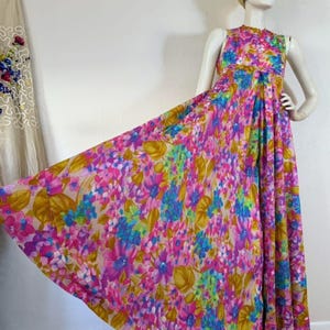 May include: A vintage floral maxi dress in shades of pink, purple, blue, and yellow. The sleeveless dress features a high neckline and a flowing skirt. The dress is displayed on a mannequin with a gold head wrap.