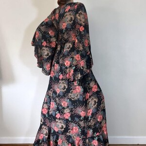 May include: A long black maxi dress with a floral print in shades of pink, blue, and gold. The dress has bell sleeves and a ruffled hem.