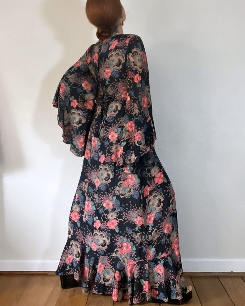 May include: A long black maxi dress with a floral print in shades of pink, blue, and gold. The dress has bell sleeves and a ruffled hem.