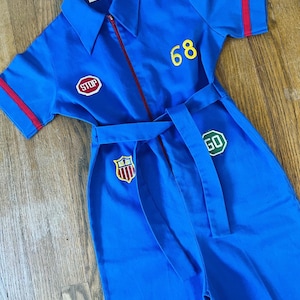 May include: A blue jumpsuit with red trim and a zipper down the front. It has a belt, and patches that say "STOP", "GO", and "68".