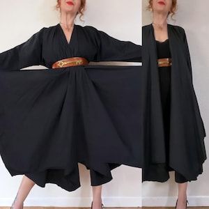以下が含まれることがあります： 深いVネックラインとフルプリーツスカートを備えた黒の長袖ドレス。ドレスは、古い鍵の形をした目立つ金色の金属製バックルが付いた幅広の茶色のレザーベルトでウエストが締められています。