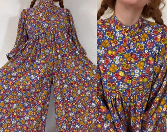 Mono vintage de los años 60 con estampado floral estilo flower power, corte imperio, pechera delantera, mangas estilo Juliette, cintura con lazo en la espalda y perneras palazzo extra anchas.