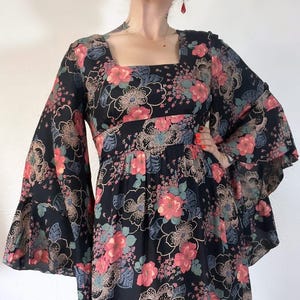 May include: A black maxi dress with a floral print featuring pink, red, and blue flowers. The dress has long bell sleeves and a square neckline.