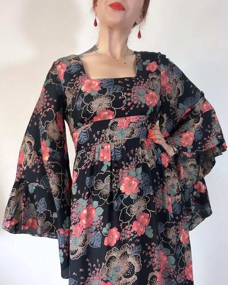 May include: A black maxi dress with a floral print featuring pink, red, and blue flowers. The dress has long bell sleeves and a square neckline.