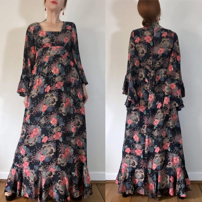 May include: A long black maxi dress with a floral print in shades of pink, blue, and gold. The dress has a square neckline, long sleeves with bell cuffs, and a ruffled hem.