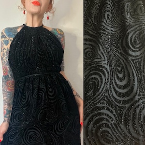 May include: A black halter dress with a swirling, glittery pattern. The dress has a fitted bodice and a flowing skirt.