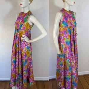 May include: A sleeveless, floor-length dress with a vibrant floral pattern in pink, blue, yellow, and green. The dress features a high neckline and a flowing skirt. A gold head wrap and white heels complete the look. The dress is displayed on a mannequin.