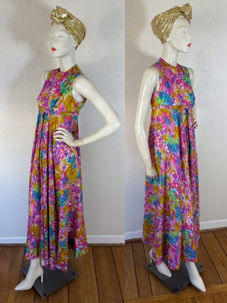 May include: A sleeveless, floor-length dress with a vibrant floral pattern in pink, blue, yellow, and green. The dress features a high neckline and a flowing skirt. A gold head wrap and white heels complete the look. The dress is displayed on a mannequin.
