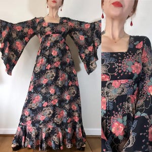 May include: A long black maxi dress with a floral print in shades of pink, green, and blue. The dress has a square neckline, long sleeves, and a flowing skirt.