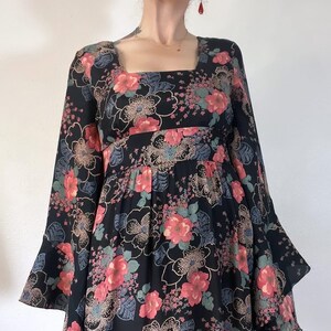 May include: A black maxi dress with a floral print featuring pink, red, and green flowers. The dress has a square neckline and long bell sleeves.