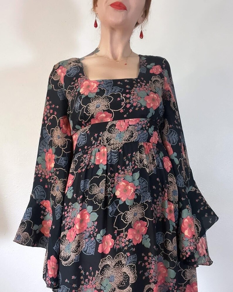 May include: A black maxi dress with a floral print featuring pink, red, and green flowers. The dress has a square neckline and long bell sleeves.