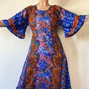 May include: A long, blue and orange maxi dress with a geometric pattern. The dress has a square neckline and bell sleeves.