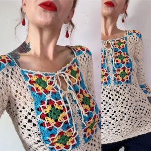 May include: A crocheted top with a square pattern in shades of blue, red, yellow, and green. The top has a tie at the neckline and long sleeves.