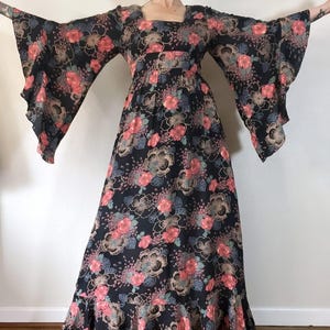 May include: A long, black maxi dress with a floral print in shades of pink, blue, and gold. The dress has a square neckline, long bell sleeves, and a ruffled hem.