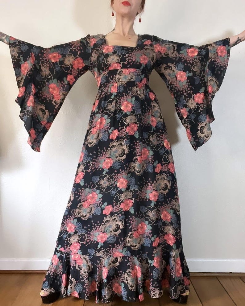 May include: A long, black maxi dress with a floral print in shades of pink, blue, and gold. The dress has a square neckline, long bell sleeves, and a ruffled hem.