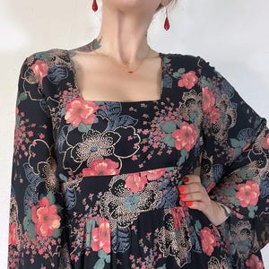 May include: A black maxi dress with a floral print and long bell sleeves. The dress has a square neckline and a fitted bodice.