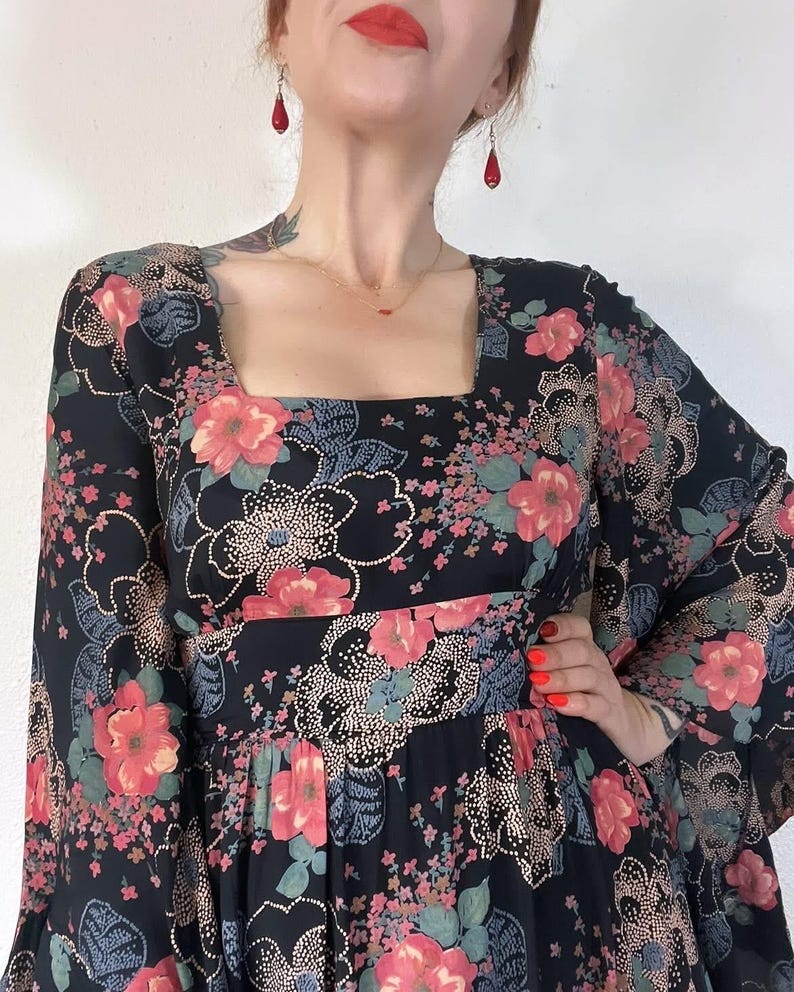 May include: A black maxi dress with a floral print and long bell sleeves. The dress has a square neckline and a fitted bodice.