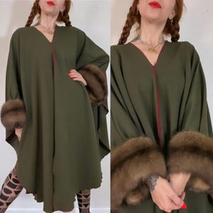 Puede incluir: Una capa verde oliva con cuello en V y ribete rojo. La capa presenta puños de piel marrón. Prenda de moda vintage.