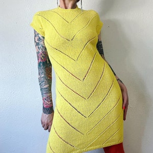 May include: A bright yellow knitted dress with a chevron pattern and short sleeves. The dress is made of a lightweight, open-knit fabric.