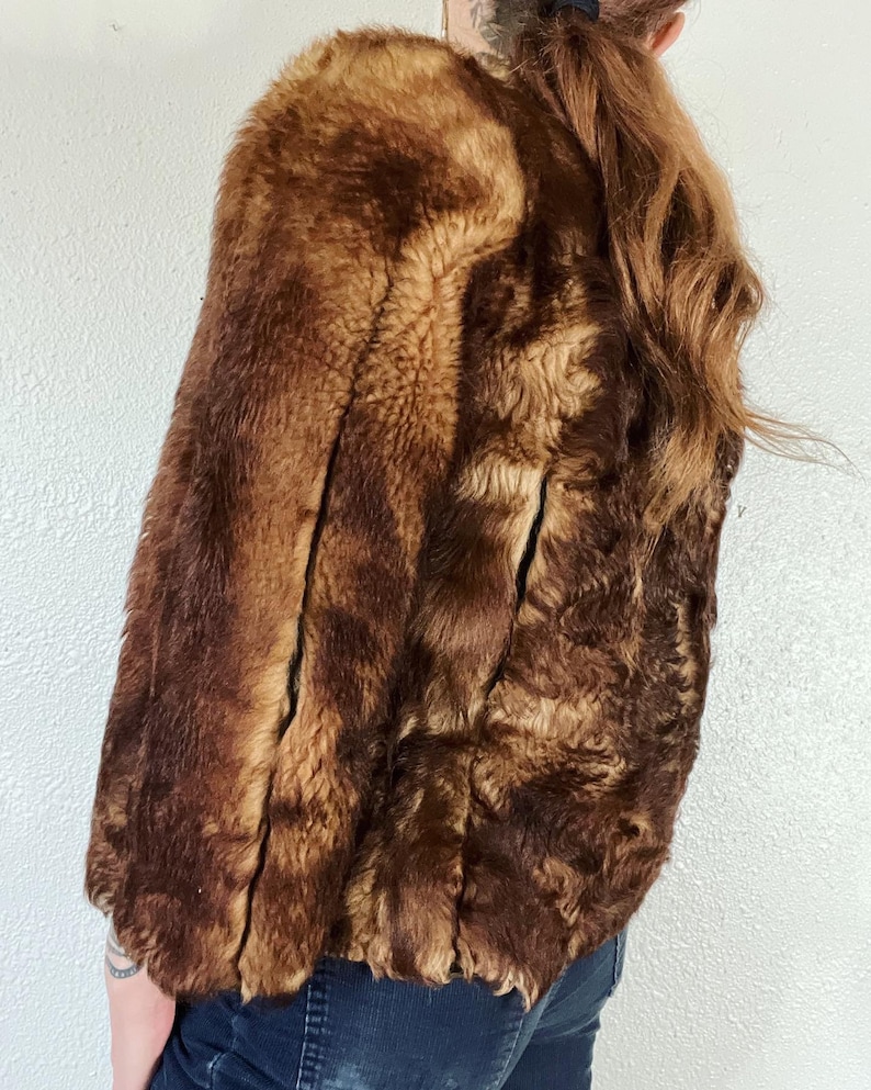 May include: A brown faux fur jacket with a shawl collar. The jacket is made of a soft, plush fabric and has a relaxed fit.