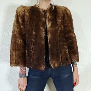 May include: A brown faux fur jacket with a stand-up collar and long sleeves. The jacket has a zipper closure and is made of a soft, plush fabric.