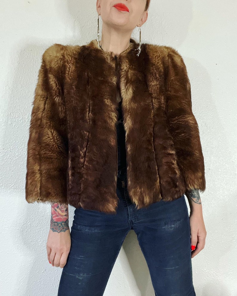 May include: A brown faux fur jacket with a stand-up collar and long sleeves. The jacket has a zipper closure and is made of a soft, plush fabric.