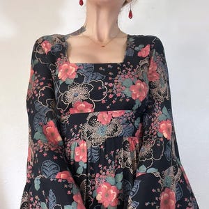 May include: A black maxi dress with a floral print featuring pink, red, and green flowers. The dress has a square neckline and long bell sleeves.